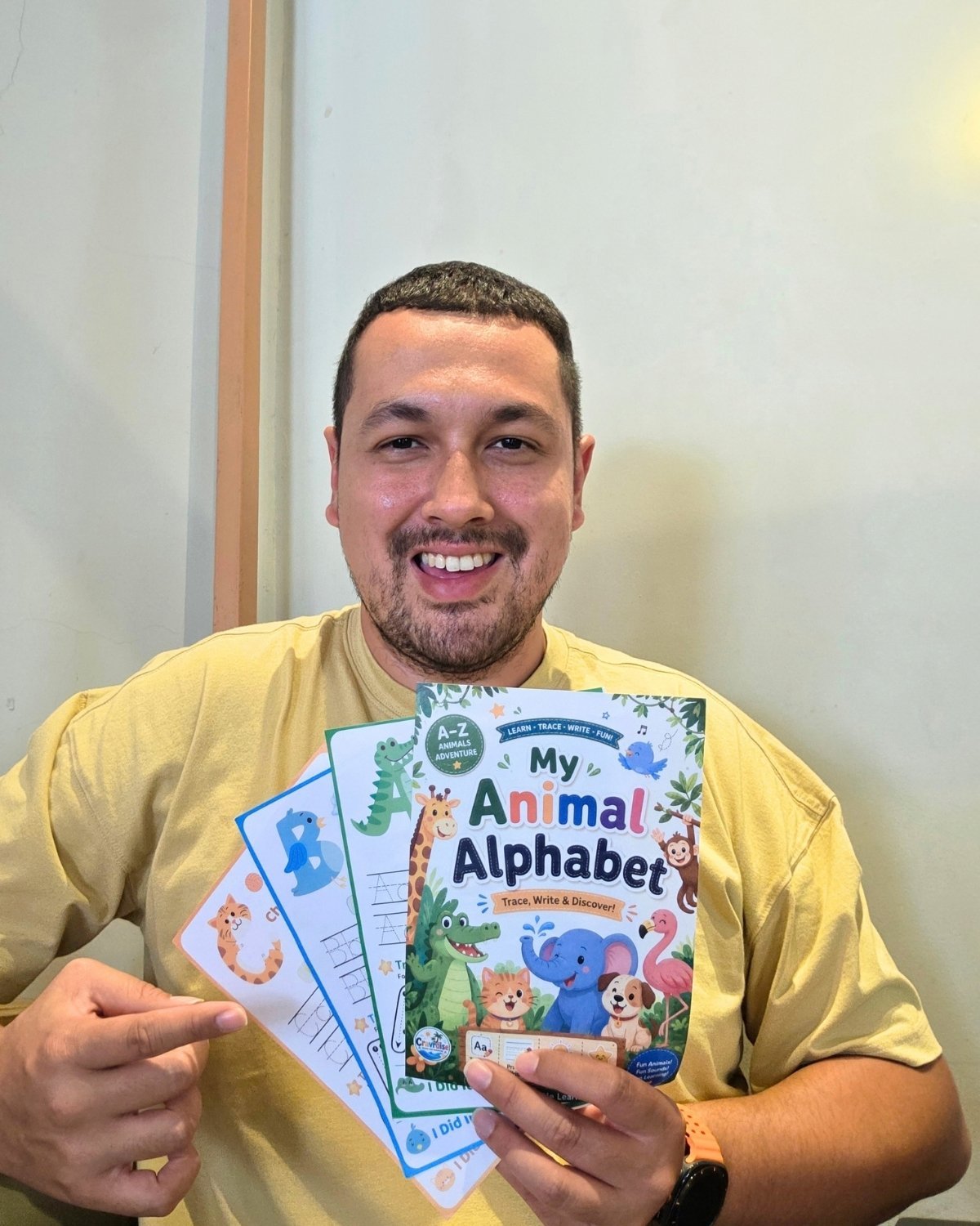 Jussi, creator of Cravrdise, smiling and holding My Animal Alphabet workbook and sample pages